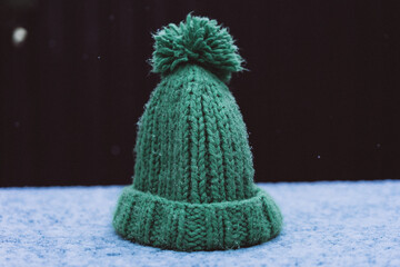 green knitted hat with a pompom covered with snow, drops from snow, first wet snow, selective focus, film and grain photo