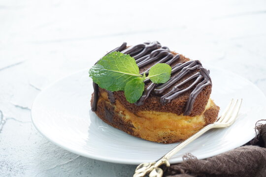 A close up picture of chocolate cheese cake in white plate and shiny background with chocolate glazing and mint leaves for food photography