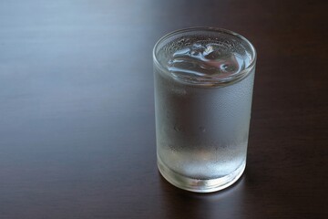 Drinking water with ice in a transparent glass on a wooden table