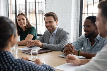 Sharing ideas. Smiling confident multiethnic employees businesspeople colleagues gathered together at conference desk brainstorming discussing marketing strategy plan engaged in talks negotiations