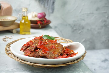 Indonesia traditional food, Dendeng Balado or beef jerky mix with chili and herbs and spices placed in white plate with lime leaves on top in the corner of the table
