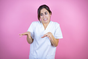 Young brunette doctor girl wearing nurse or surgeon uniform over isolated pink background disgusted...