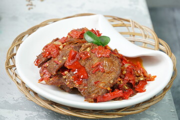 Indonesia traditional food, Dendeng Balado or beef jerky mix with chili and herbs and spices placed in white plate with lime leaves on top in the corner of the table