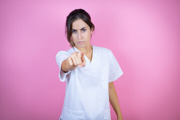 Young brunette doctor girl wearing nurse or surgeon uniform over isolated pink background pointing to the front with finger