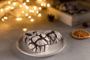 homemade chocolate crinkle cookies in white plate against blurred christmas lights. cozy home atmosphere. close-up.