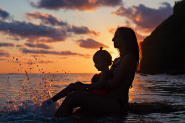 Happy people have fun on summer beach holiday. Young mother with daughter relax at sea water pool. Looking at beautiful view of sunset sky. Healthy family lifestyle, summer travel on tropical island.