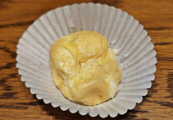 Choux cream in white paper baking cup on wooden table.
