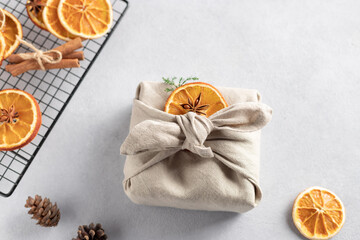Christmas gift wrapped in linen cloth and decorated with dried orange and anise. Furoshiki Japanese Gift fabric Wrapping. Gray background. copy space. soft focus