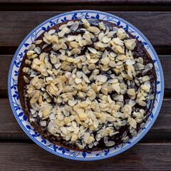 Cocoa and coconut cake covered with chocolate glaze and almond flakes, on wooden background