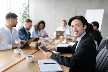 Happy Asian Businessman Using Tablet Sitting With Colleagues In Office