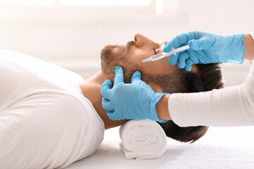 Bearded man getting beauty injection in face in luxury salon