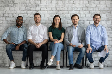Fototapeta premium Portrait of happy multiethnic clients customers sitting in row looking at camera satisfied with service received, signing loan mortgage insurance agreement, diverse applicants are glad of getting job
