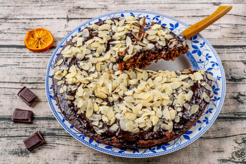 Cocoa and coconut cake covered with chocolate glaze and almond flakes, with a slice cut