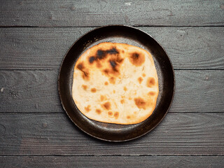 Fresh naan bread in cast-iron pan on dark wooden background with copy space. Top view of perfect naan flatbread black circle cast iron pan