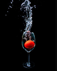 A red tomato dropped on a wine glass filled with water to create a big splash and shot on a black background