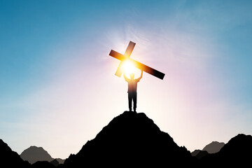 Silhouette Human holding cross or Crucifixion of Jesus Christian on top of mountain with sunlight...