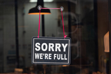 Text on vintage black sign "Sorry we're full " in cafe.