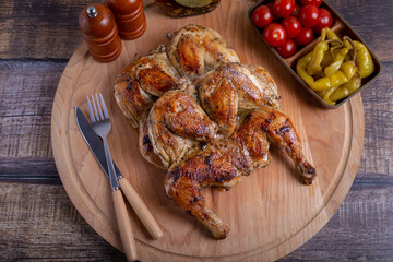 Tapaca (tabaca) chickens with cherry tomatoes and pepperoni on a wooden board. Traditional Georgian dish. Close-up.