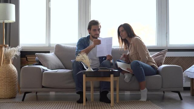 Frustrated young adult couple feeling stressed about high mortgage rates doing paperwork at home. Angry husband and wife renters calculating household payments, having financial problems or bank debt.