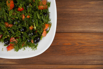 Dill, tomatoes and olives salad in plate, wooden background. Vitamin, summer, recipe, menu concept. Top view, flat lay, copy space