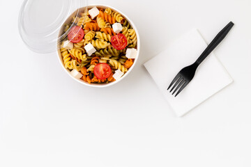 Pasta with tomato and feta in taking away box on white table