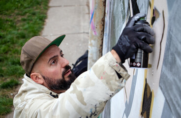 Street graffiti artist in action, drawing  with spray paint can on the wall in rainy weather. Street art culture concept. Top view.