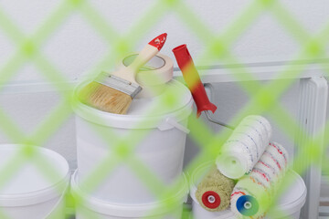 Fototapeta na wymiar a set of tools for painting the surface, against the background of a green mesh, rollers, buckets, paints, stairs