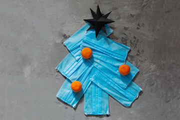 Christmas tree made from face masks with orange tangerine decor on grey concrete background. New year's eve 2021 in the context of the coronovirus pandemic, lockdown quarantine.