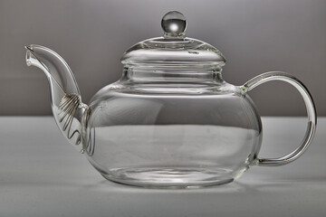 Empty glass teapot on gray background close up