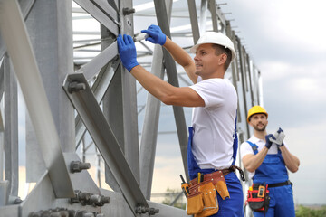 Workers building high voltage tower construction outdoors. Installation of electrical substation