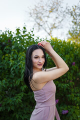 Beautiful dark-haired model posing among blossoming lilac bushes on spring background.