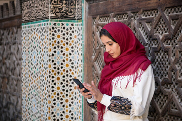 Muslim woman writing a message on a mobile phone in traditional clothing with red headscarf on her head