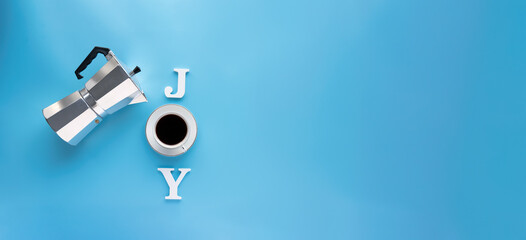 Mocha coffee maker and coffee cup on the inscription JOY  made up over blue background.
