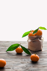 Still life composition of fresh harvested tangerines with green leaves on burlap and wooden...