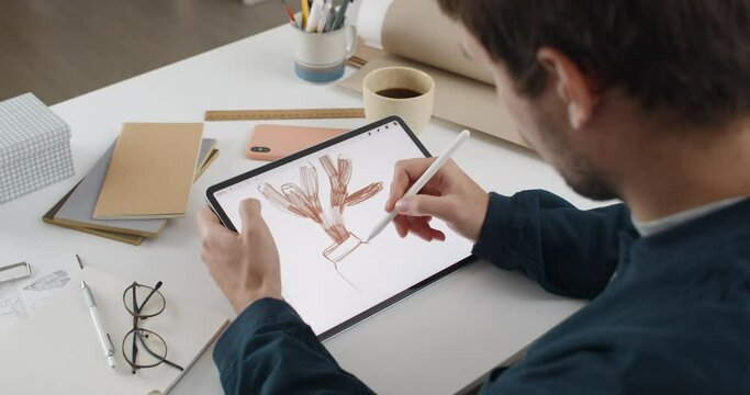 Over shoulder view of fmale artist drawing plant while creating illustration on tablet.Man graphic illustrator using digital pad and stylus while sitting at desk. Concept of modern art