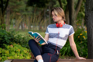 Young gay man reading a book in a park