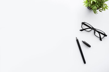 White office desk table with pen, eye glasses and green plant pot. Top view with copy space, flat lay.