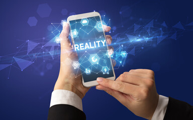 Female hand holding smartphone with REALITY inscription, modern technology concept