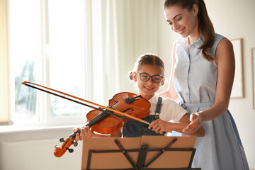 Young woman teaching little girl to play violin indoors