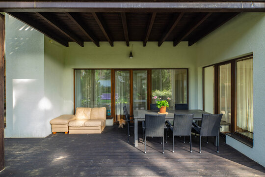 Outdoor terrace with table and chairs. Flower on table. Private house. Panorama windows and glass door.
