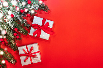 Xmas festive background with fir branches covered by snow, red berries, two DIY gift boxes tied with ribbons and bows on red. Christmas invitation or greeting card. Top view, copy space for text.