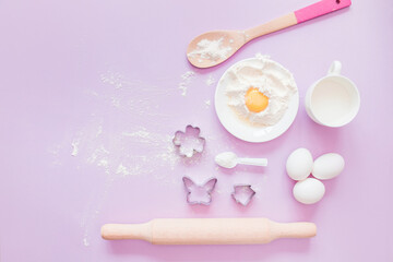 Obraz na płótnie Canvas Baking ingredients. Eggs, flour, milk, whisk, rolling pin, bakeware on a lilac background, top view. cook's workplace in the kitchen. beautiful dishes. Copy space. homemade cookies. Cooking background
