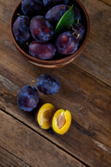 Blue plum in a bowl on a wooden table. Plums in a cut. Top view, place for text. Fruit background with copy space. Still life food.
