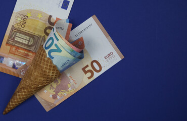 Close up of ice cream waffle cone with rolled up euro paper banknotes - financial aid support gift concept