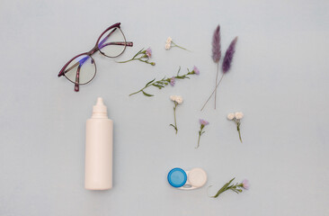 glasses, contact lenses, container on a light blue background with flowers. eye health concept, optics. Ophthalmologist tools. texture for the optometrist. choice of glasses or lenses