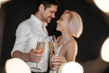 Beautiful happy couple young family in evening dresses with glasses of champagne on the dark background, selective focus