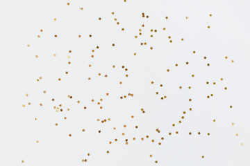 Spangles of gold and silver are scattered from bottles on a white background