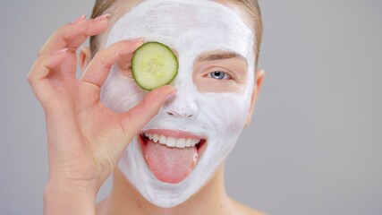 Extreme Closeup Portrait Young Caucasian Beautiful Blonde Woman With Blue Eyes She Covering Eye Fresh Cucumber White Mask Cosmetic On Face And Smiling On Gray Background Skin Care Concept