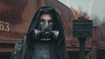 Woman in grunge suit with burning torch in her hand standing by rusty train carriage and looking into camera. Dystopian warrior concept, female survivor in abandoned city. Post apocalyptic world - Powered by Adobe