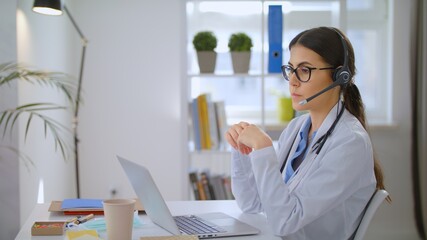 Young Female Doctor Wears White Coat, Video Calling Distant Patient on Laptop. Doctor Talking to...